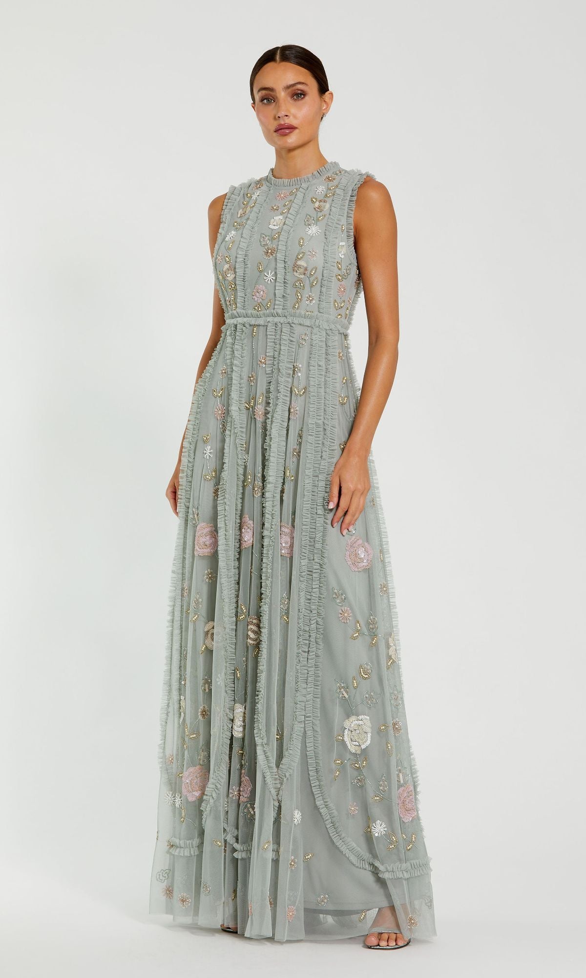 A woman stands against a plain white background wearing the Sleeveless Long Sage Formal Dress: Mac Duggal 9360, featuring floral embroidery and a sheer overlay.